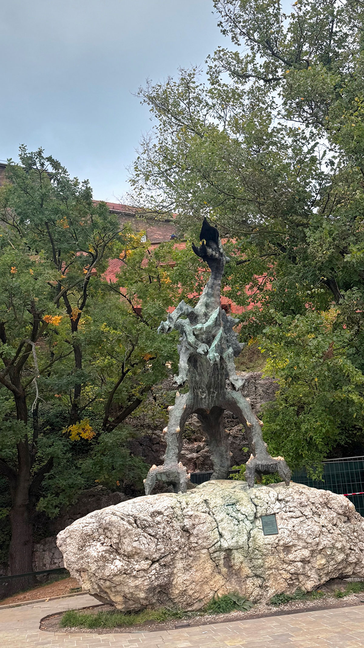 The Wawel Dragon statue under the castle hill in Krakow, surrounded by green trees